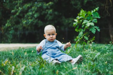 Tişört ve kot pantolon giyen bir yaşında sarışın bir çocuk temiz havada yürür. Çocuğun kişisel gelişimi.