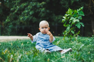 Tişört ve kot pantolon giyen bir yaşında sarışın bir çocuk temiz havada yürür. Çocuğun kişisel gelişimi.