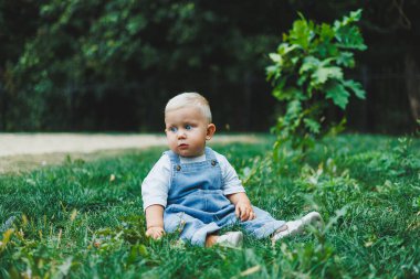 Tişört ve kot pantolon giyen bir yaşında sarışın bir çocuk temiz havada yürür. Çocuğun kişisel gelişimi.