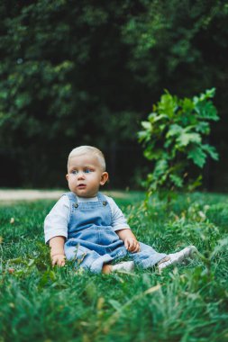 Tişört ve kot pantolon giyen bir yaşında sarışın bir çocuk temiz havada yürür. Çocuğun kişisel gelişimi.