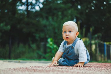 Tişört ve kot pantolon giyen bir yaşında sarışın bir çocuk temiz havada yürür. Çocuğun kişisel gelişimi.