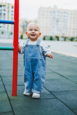 Tişört ve kot pantolon giyen bir yaşında sarışın bir çocuk temiz havada yürür. Çocuğun kişisel gelişimi.