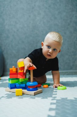 Küçük bir çocuk halıya oturur ve tahta bir piramitle oynar. Bebeğin gelişimi. Bebekler için oyuncaklar