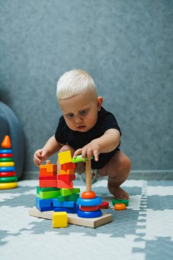 Küçük bir çocuk halıya oturur ve tahta bir piramitle oynar. Bebeğin gelişimi. Bebekler için oyuncaklar