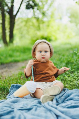 1 yaşında bir çocuk çimlerin üzerinde oturur ve su içer. Yazın temiz havada bir bebek yürüyüşü. Bir çocuk için piknik.