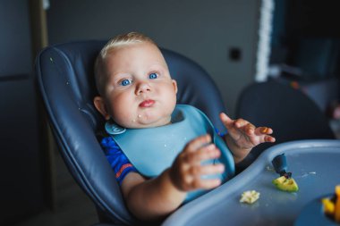 Küçük bir çocuk çatalla yemek yemeyi öğreniyor. Bebek maması. Çocuk kendi başına yemek yemeyi öğreniyor..