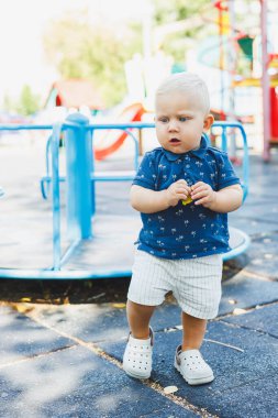Oyun sahasında şortlu ve tişörtlü küçük bir çocuk oynuyor. Sokakta oynarken bir çocuk koşar ve gülümser..