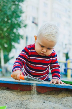 Bir yaşında sarışın bir çocuk kum havuzunda oynuyordu. Çocuğun kişisel gelişimi.