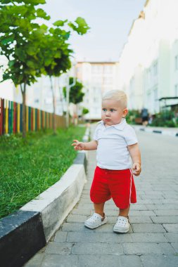 Yazın yürüyüşe çıkan beyaz tişörtlü ve şortlu bir çocuk. Çocuk koşuyor ve temiz havada oynuyor..