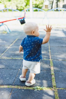 Oyun parkında mavi tişörtlü ve şortlu küçük bir çocuk koşuyor. Çocuk aktif olarak oynayarak ve temiz havada yürüyerek zaman geçirir..
