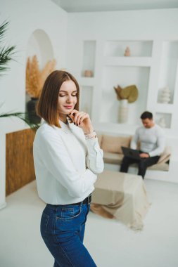 Evdeki parlak bir odada sevimli bir kadın duruyor. Günlük giysiler içinde bir kadın evde dinleniyor..