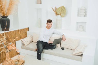 Beyaz kazaklı bir adam evde dizüstü bilgisayar üzerinde çalışıyor. Erkek serbest çalışan uzaktan kumandalı..