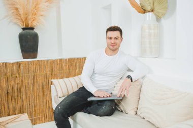 Beyaz kazaklı bir adam evde dizüstü bilgisayar üzerinde çalışıyor. Erkek serbest çalışan uzaktan kumandalı..