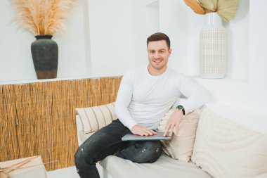 Beyaz kazaklı bir adam evde dizüstü bilgisayar üzerinde çalışıyor. Erkek serbest çalışan uzaktan kumandalı..