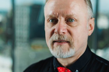 Siyah gömlekli, piercingli yaşlı bir adam. Sakallı bir iş adamının yakın plan portresi.