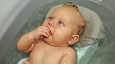 Kürsüde yatarken bebeği banyoda yıkamak. İlk bebek banyosu. Bebek hijyeni. 3 aylık bir bebek banyoda yatıyor.