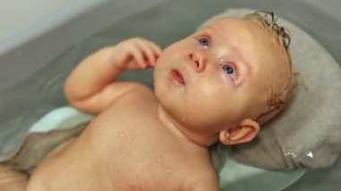 Kürsüde yatarken bebeği banyoda yıkamak. İlk bebek banyosu. Bebek hijyeni. 3 aylık bir bebek banyoda yatıyor.