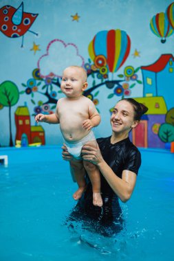 Çocuk bir yıldır havuzda bir koçla birlikte yüzüyor. Bir çocuğa yüzmeyi öğretmek. Çocuklar için yüzme havuzu.