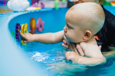 Bir koç erkek bebeğe yüzmeyi öğretir. Çocuklara yüzme öğretmek için yüzme havuzu.
