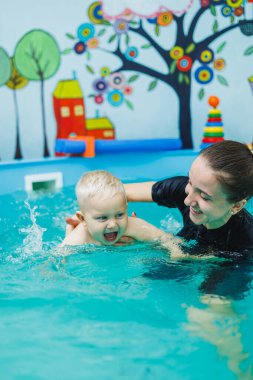 Bir çocuk bir çocuk havuzunda annesiyle birlikte yüzer. Bir anne küçük oğluna yüzmeyi öğretir..