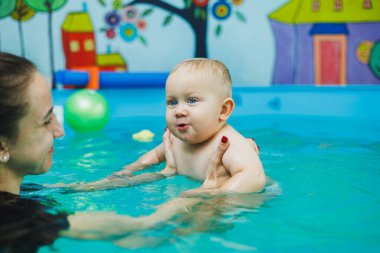 Bir çocuk bir çocuk havuzunda annesiyle birlikte yüzer. Bir anne küçük oğluna yüzmeyi öğretir..
