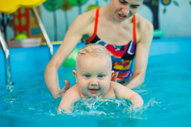 Bir bebek bir antrenörle havuzda yüzmeyi öğrenir. Çocuk havuzu. Çocuklar için yüzme kursları.