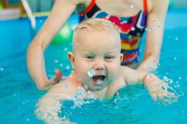 Bir bebek bir antrenörle havuzda yüzmeyi öğrenir. Çocuk havuzu. Çocuklar için yüzme kursları.