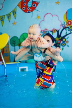 Bir bebek bir antrenörle havuzda yüzmeyi öğrenir. Çocuk havuzu. Çocuklar için yüzme kursları.
