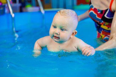 Bir bebek bir antrenörle havuzda yüzmeyi öğrenir. Çocuk havuzu. Çocuklar için yüzme kursları.