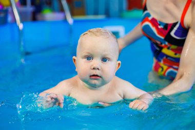 Bir bebek bir antrenörle havuzda yüzmeyi öğrenir. Çocuk havuzu. Çocuklar için yüzme kursları.