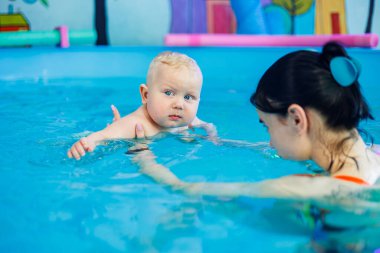 Küçük bir çocuk bayan bir koçla havuzda yüzmeyi öğreniyor. Bebek havuzda yüzüyor..