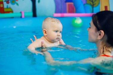 Küçük bir çocuk bayan bir koçla havuzda yüzmeyi öğreniyor. Bebek havuzda yüzüyor..