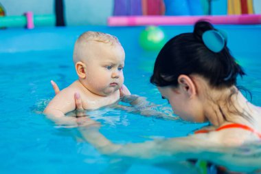 Küçük bir çocuk bayan bir koçla havuzda yüzmeyi öğreniyor. Bebek havuzda yüzüyor..