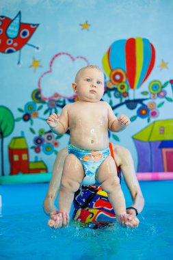 Erkek çocuk havuzda yüzüyor. Bir antrenör bebeğe yüzmeyi öğretir..