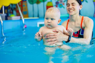 Erkek çocuk havuzda yüzüyor. Bir antrenör bebeğe yüzmeyi öğretir..