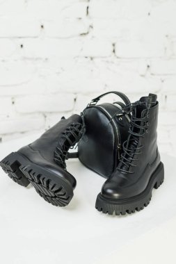 Kadınların siyah deri çizmeleri ve beyaz arka planda siyah deri bir sırt çantası var. Kadın modası