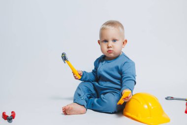 Beyaz arka plandaki bebek, plastik çekiçle oynuyor. İnşaat için çocuk aletleri. Çocuk beyaz arka planda oyuncaklarla oynuyor
