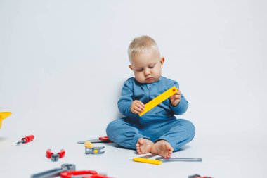 Beyaz arka plandaki bebek, plastik çekiçle oynuyor. İnşaat için çocuk aletleri. Çocuk beyaz arka planda oyuncaklarla oynuyor