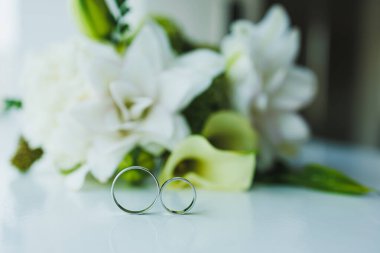 Çiçeklerin arka planında yeni evliler için altın alyanslar. Gelin ve damat için değerli altın alyanslar..