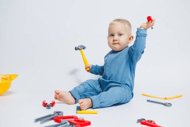 Beyaz arka plandaki bebek, plastik çekiçle oynuyor. İnşaat için çocuk aletleri. Çocuk beyaz arka planda oyuncaklarla oynuyor