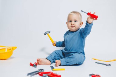 Beyaz arka plandaki bebek, plastik çekiçle oynuyor. İnşaat için çocuk aletleri. Çocuk beyaz arka planda oyuncaklarla oynuyor