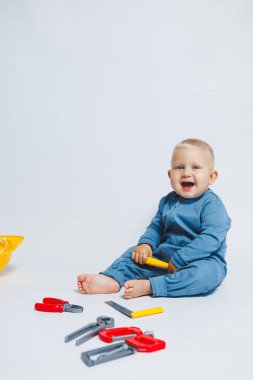 Beyaz arka plandaki bebek, plastik çekiçle oynuyor. İnşaat için çocuk aletleri. Çocuk beyaz arka planda oyuncaklarla oynuyor