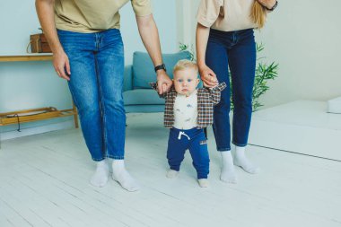 Küçük çocuk anne ve babasıyla el ele yürümeyi öğreniyor. İlk adımları atan çocuk.