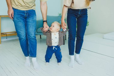 Küçük çocuk anne ve babasıyla el ele yürümeyi öğreniyor. İlk adımları atan çocuk.