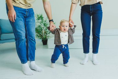 Küçük çocuk anne ve babasıyla el ele yürümeyi öğreniyor. İlk adımları atan çocuk.