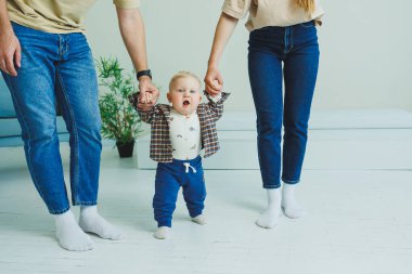 Küçük çocuk anne ve babasıyla el ele yürümeyi öğreniyor. İlk adımları atan çocuk.
