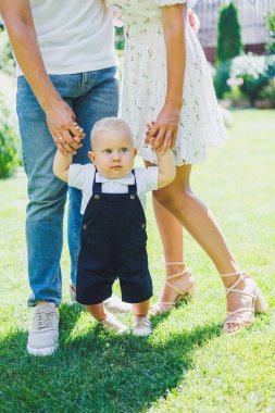 Küçük çocuk anne ve babasıyla el ele yürümeyi öğreniyor. İlk adımları atan çocuk.