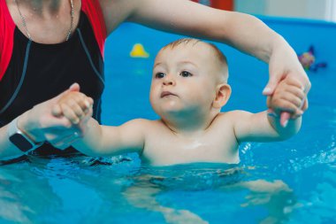 1 yaşındaki bir çocuk bir koçla çocuk havuzunda yüzmeyi öğreniyor. Çocuklar için yüzme kursları. Çocuk havuzu.
