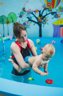 1 yaşındaki bir çocuk bir koçla çocuk havuzunda yüzmeyi öğreniyor. Çocuklar için yüzme kursları. Çocuk havuzu.