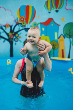 1 yaşındaki bir çocuk bir koçla çocuk havuzunda yüzmeyi öğreniyor. Çocuklar için yüzme kursları. Çocuk havuzu.